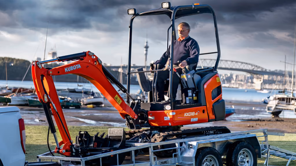 Orange Kubota excavator with tracked undercarriage and digging arm.