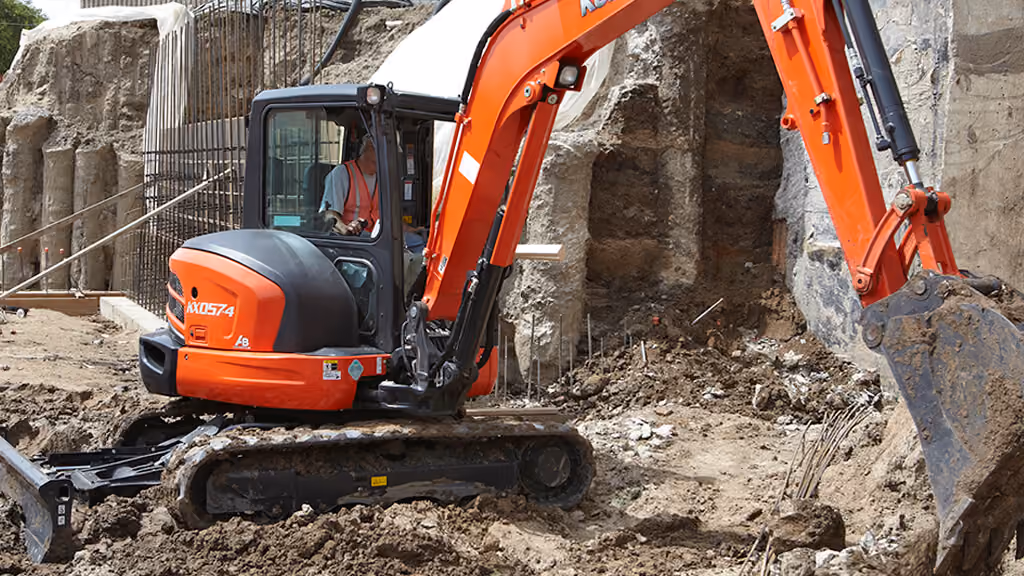 Orange Kubota excavator with tracked undercarriage and digging arm.
