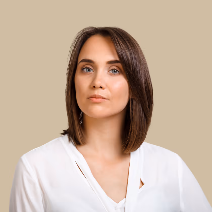 Serious woman with brown hair wearing a white blouse against a beige background.