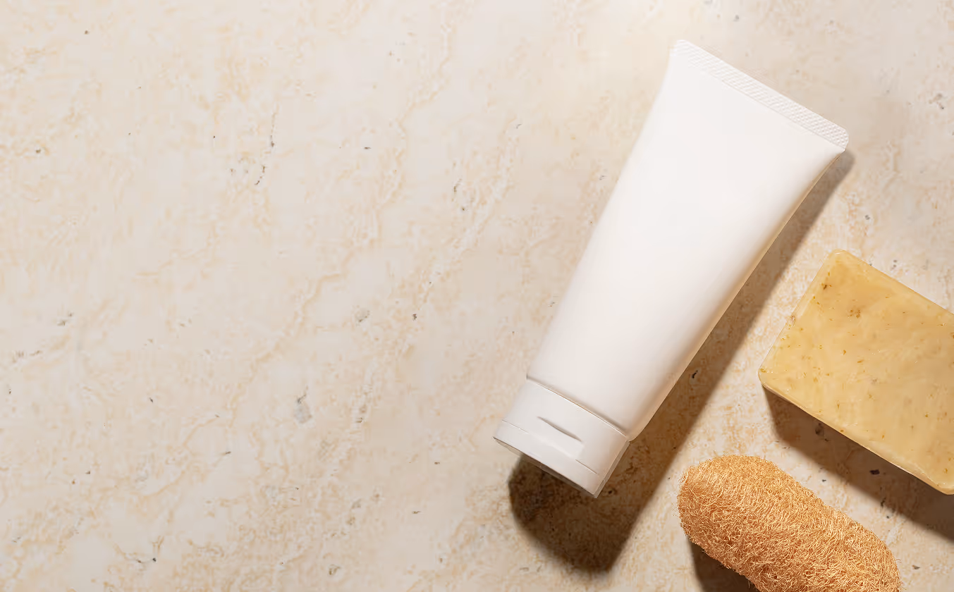 White tube, beige soap bar, and natural loofah on marble surface.