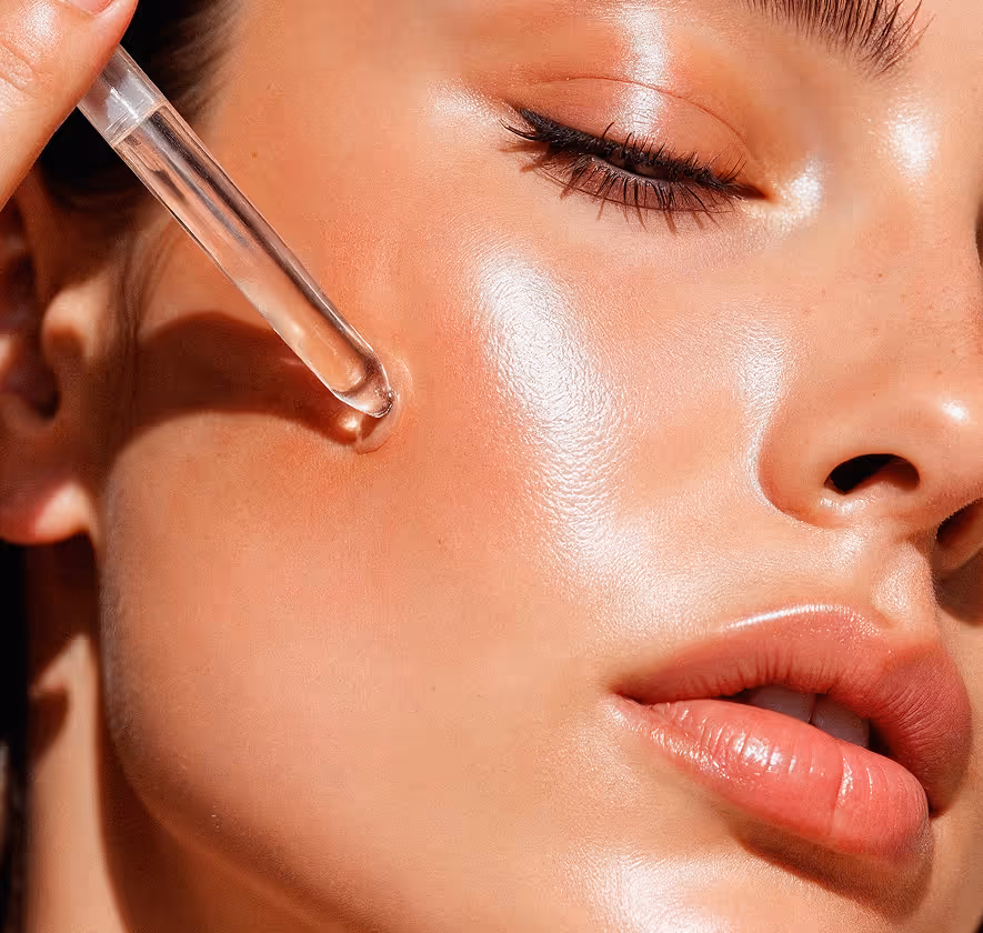 Close-up of a woman applying clear serum to her glowing, smooth cheek with a dropper.