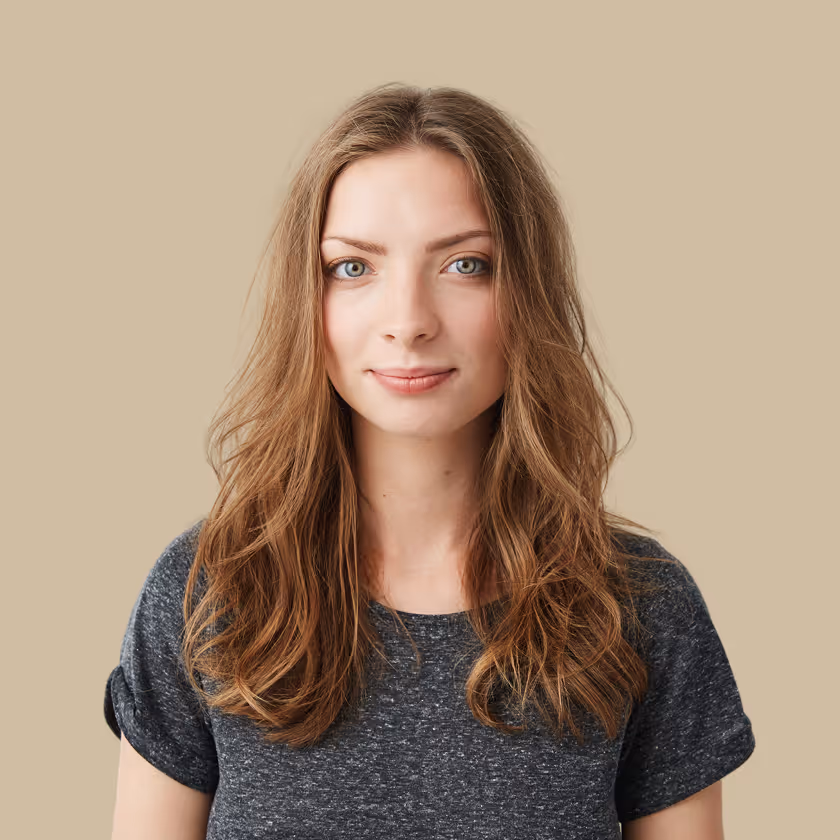 Woman with long brown hair and light eyes wearing a dark gray t-shirt on a beige background.