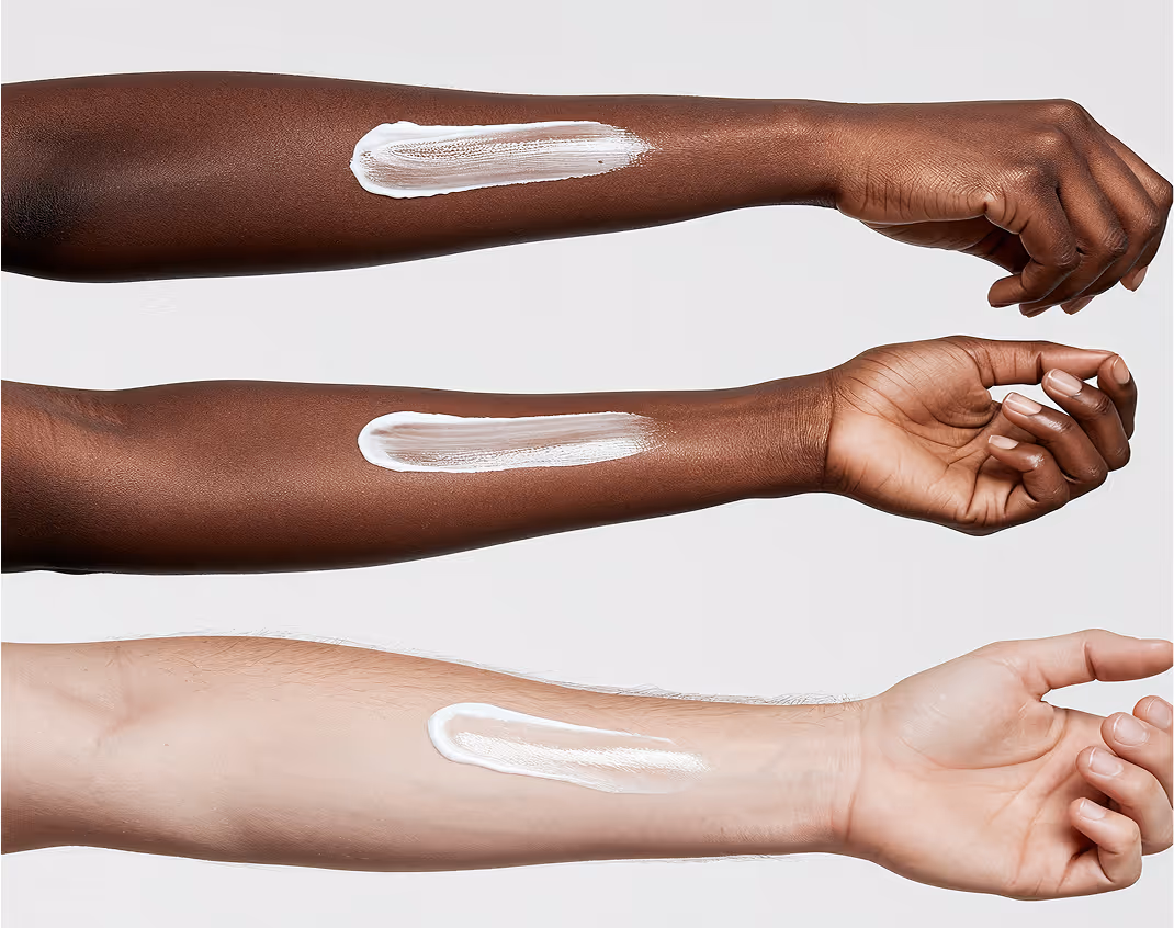 Three arms with different skin tones, each with a white cream swatch applied on the forearm.