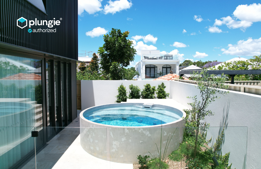 Plungie Arena 11'5" round precast concrete pool installed above-ground with clean render surround, glass fencing, and lush landscaping — installed by DropIn Oasis Pools, Houston's authorized Plungie installer.
