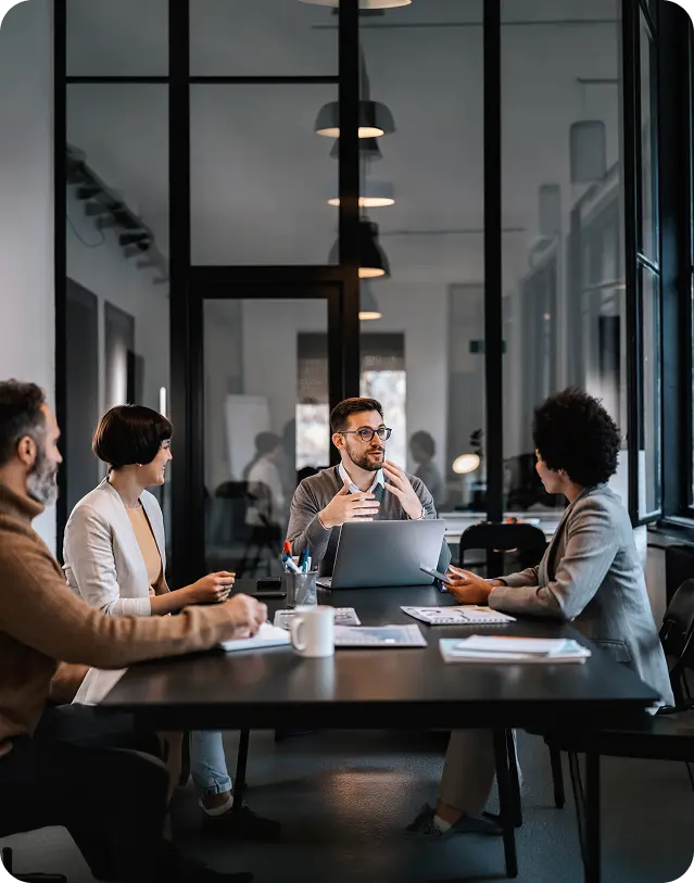 Four professionals having a meeting around a table with laptops and documents in a modern office.
