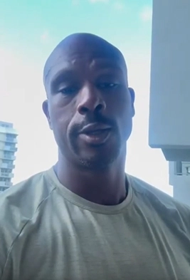 Man wearing light gray shirt standing outside with buildings and blue sky in the background.