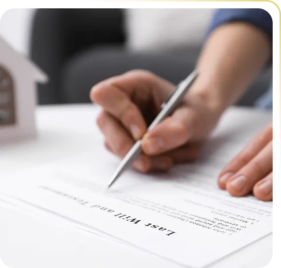 Person signing a last will and testament document at a white table with a house model nearby.