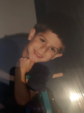 Smiling young boy resting his chin on his hand against a dark background.