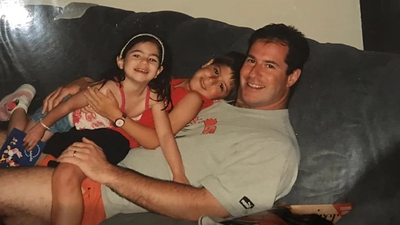 Man sitting on couch smiling with two children lying on his lap and hugging him.