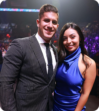 Smiling man in pinstripe suit and woman in blue dress posing together at a dark event with purple lights.