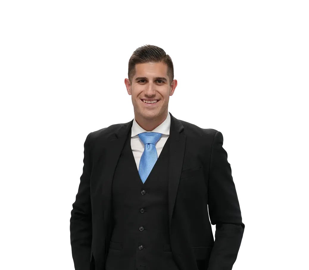 Smiling man in a black suit, white shirt, and blue tie standing against a transparent background.