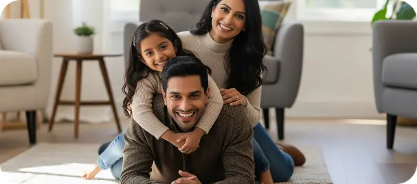 Smiling family of three with daughter hugging father, sitting on floor in a bright living room.