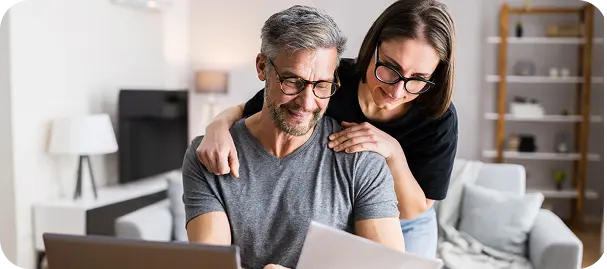 Middle-aged man and woman wearing glasses reviewing documents together in a modern living room.