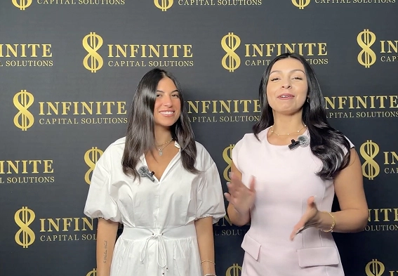 Two women standing and talking in front of an Infinite Capital Solutions branded backdrop.