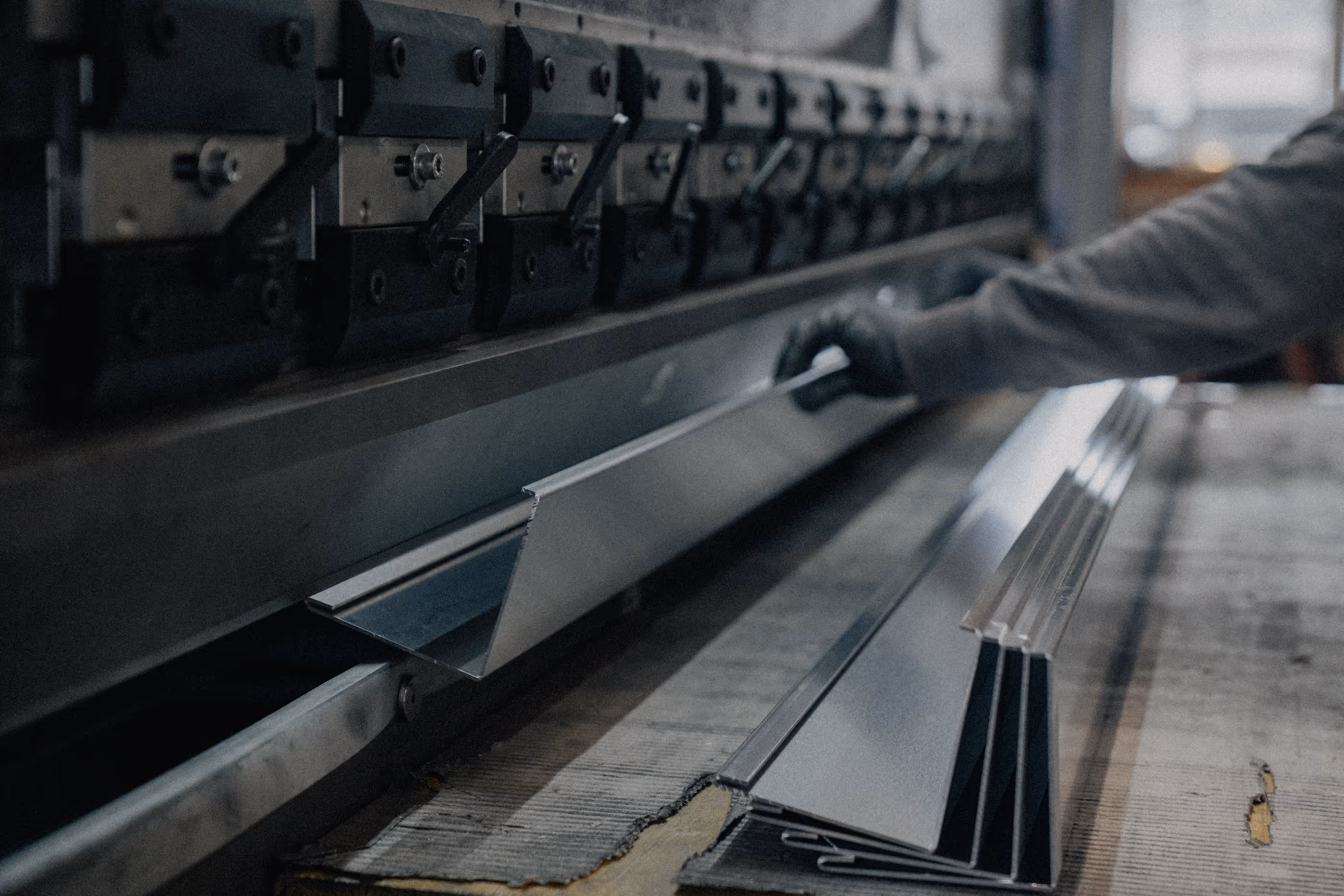Person operates a metal bending machine shaping angled metal sheets in an industrial setting.
