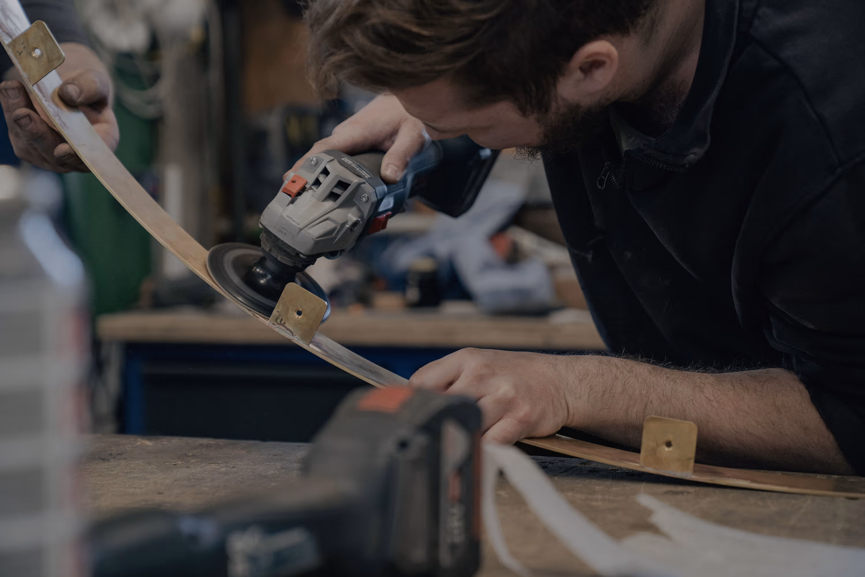 Person schleift ein gebogenes Metallband mit einem Winkelschleifer in einer Werkstatt.