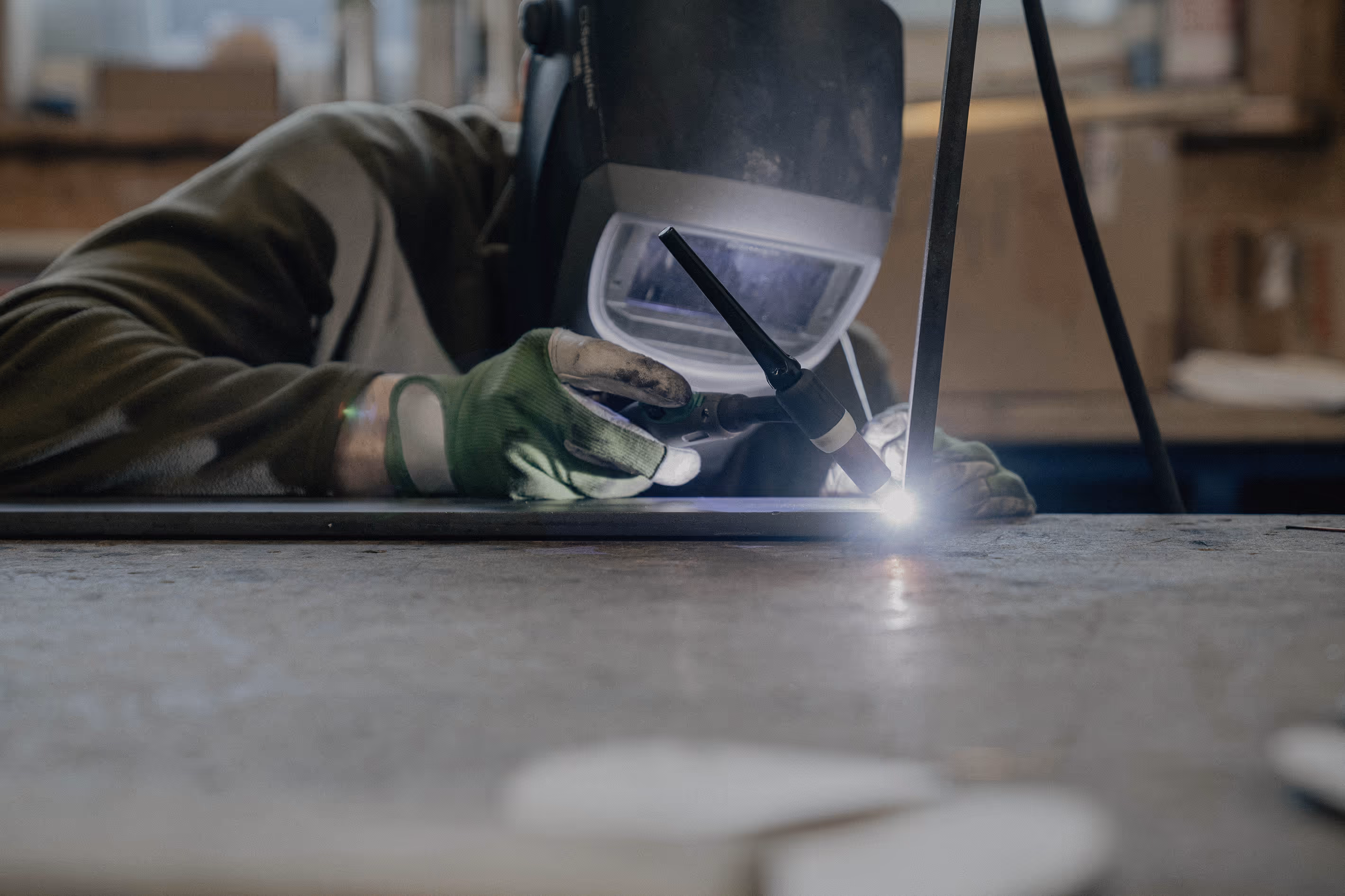 Person mit Schweißhelm und Handschuhen, der Metall mit Schweißgerät verbindet.