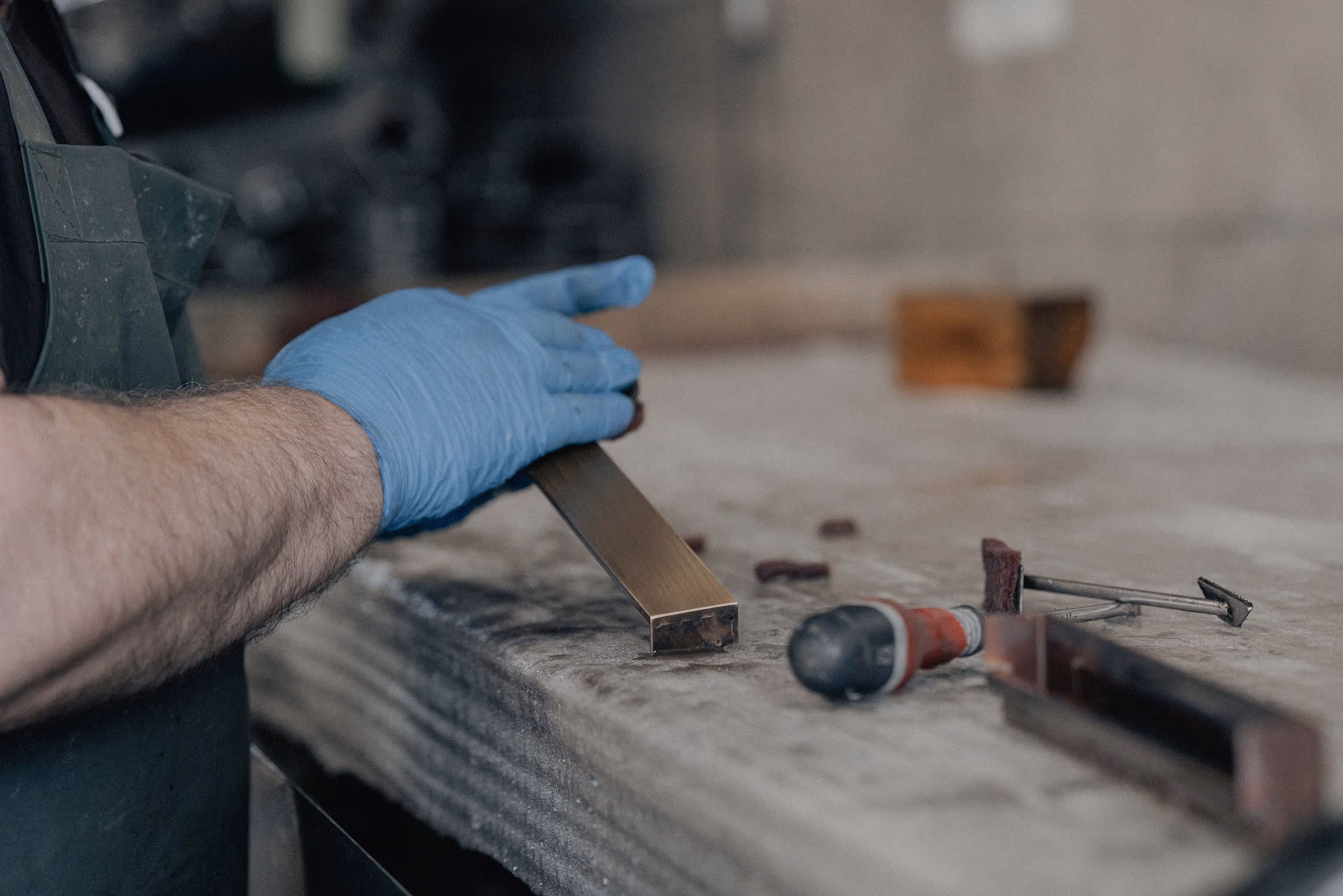 Hand mit blauer Schutzhandschuharbeit poliert ein Metallstück auf einer Werkbank.