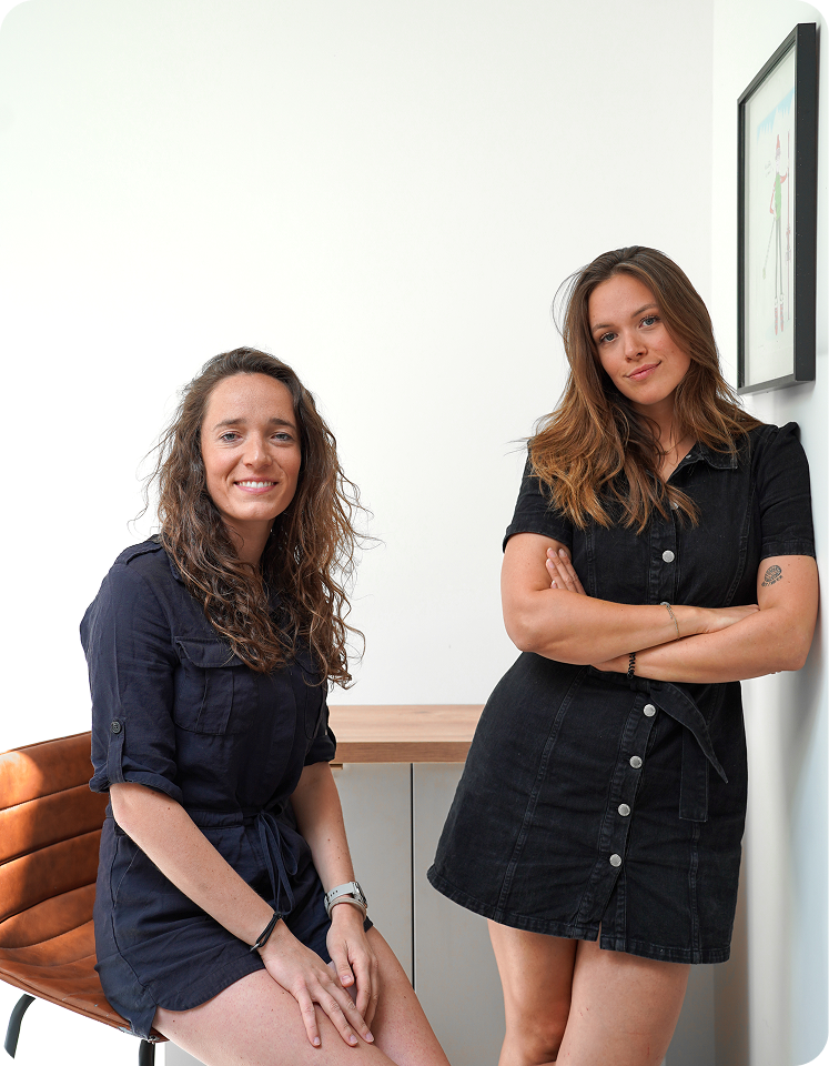 Les deux fondatrices, sérieuses, regardent un ordinateur portable Apple dans une pièce avec meubles en bois.