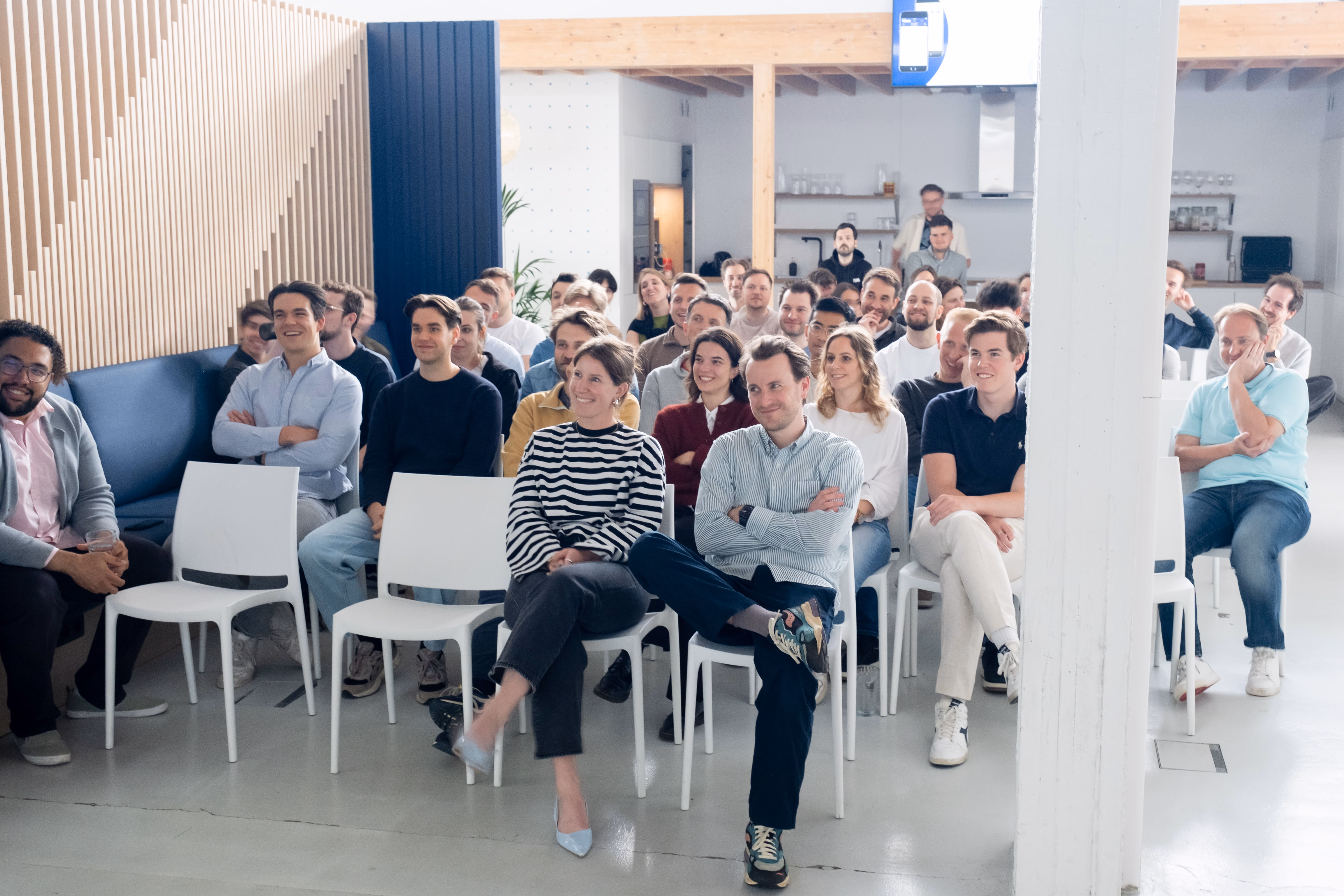 Group of people attentively listening to a speaker presenting in a modern room with large window.