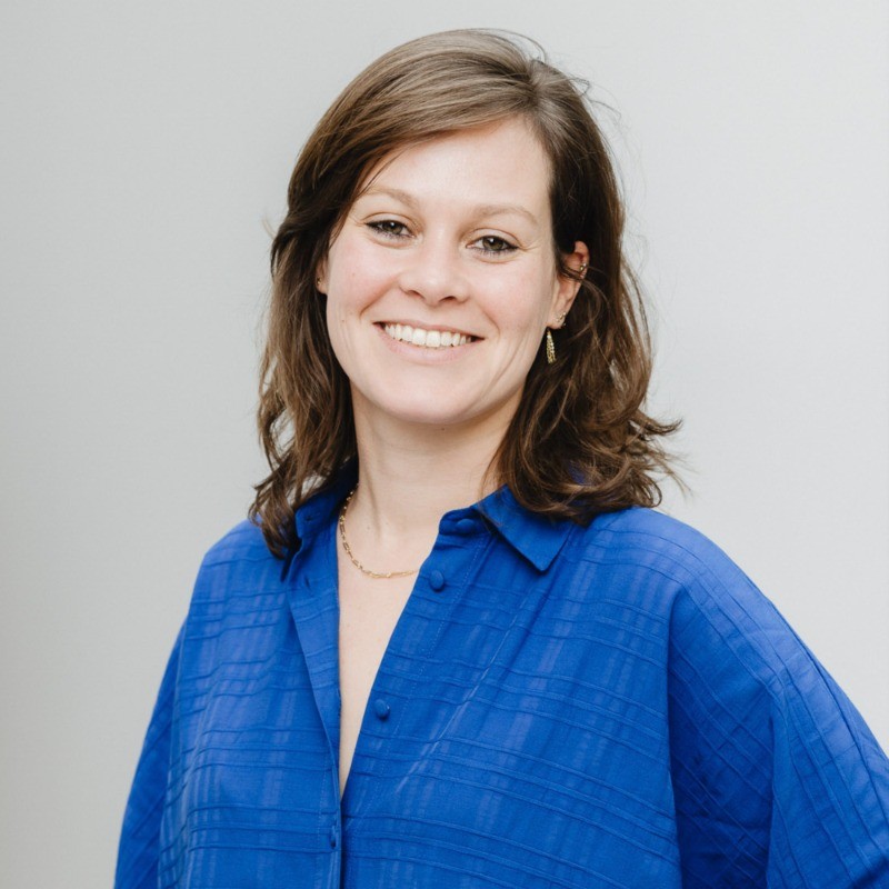 Smiling woman with shoulder-length brown hair wearing a blue button-up shirt and small jewelry.