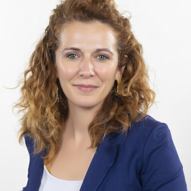 Woman with curly light brown hair wearing a blue blazer and white top against a white background.