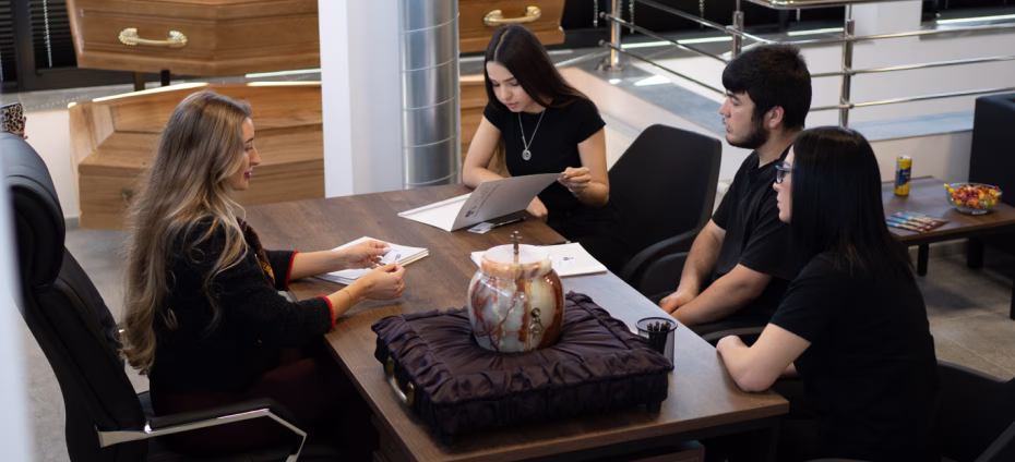 Four young adults sitting around a table with documents, engaged in discussion in a modern room.
