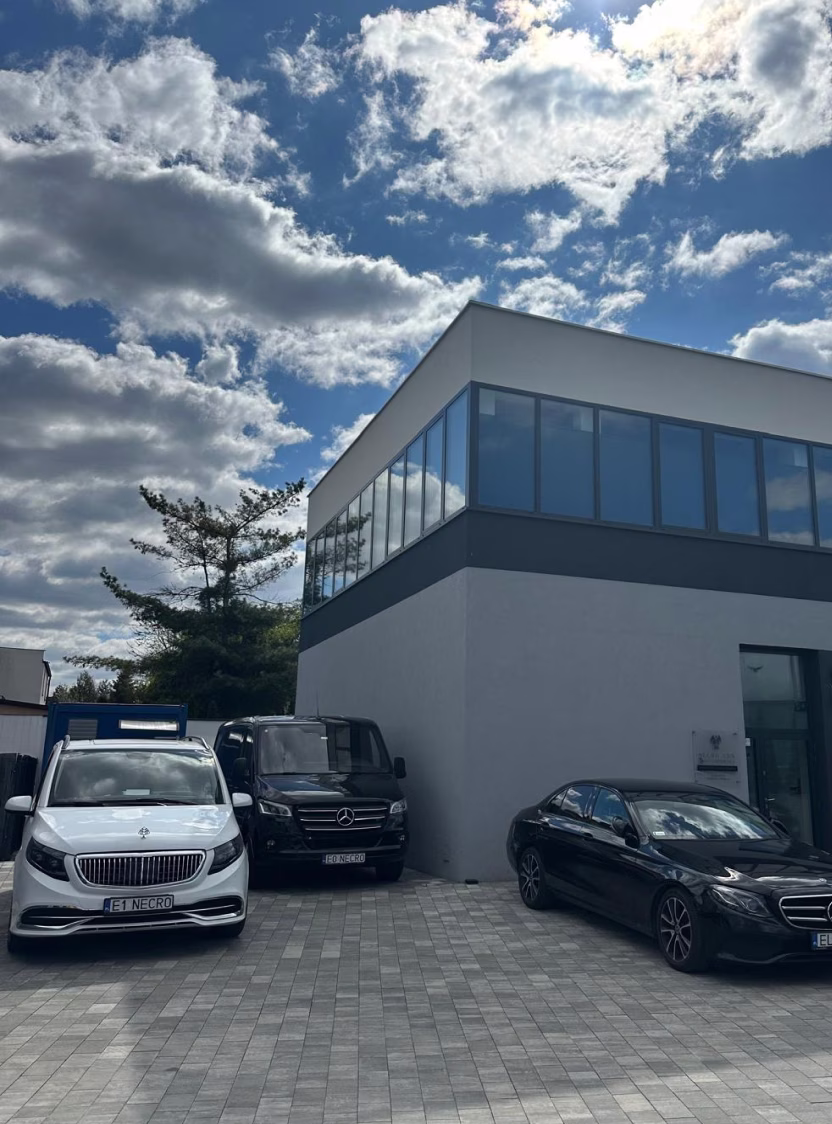 Three Mercedes vehicles parked outside a modern two-story building under a cloudy sky.