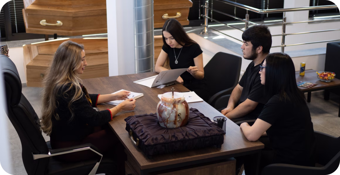 Four people seated around a table discussing documents, with a decorative urn centerpiece.