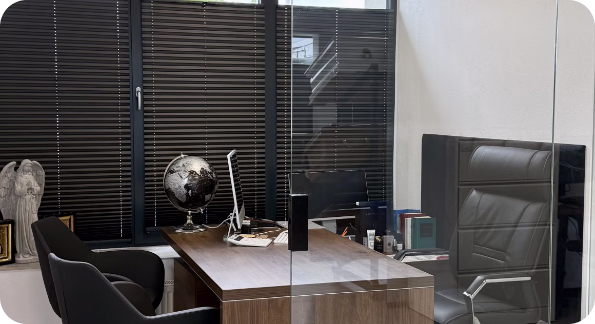 Modern office with wooden desk, black chairs, a globe, computer, and closed window blinds.
