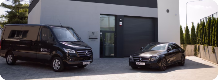 Чорний фургон і легковий автомобіль Mercedes-Benz біля сучасної будівлі з великими дверима