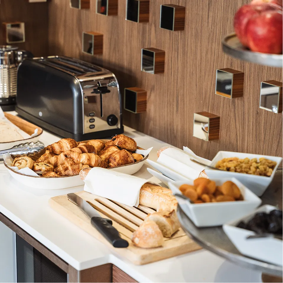 Table with croissants, baguettes, dried fruits, canned food, and a toaster on a kitchen counter.