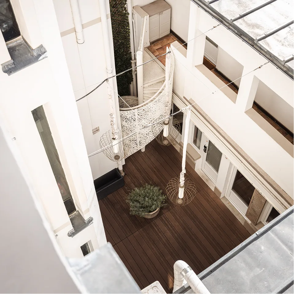 Cour intérieure moderne avec escalier en colimaçon blanc, suspension design et plante sur terrasse en bois.