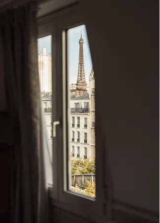 Vue de la tour Eiffel à travers une fenêtre encadrée par un mur et un rideau.