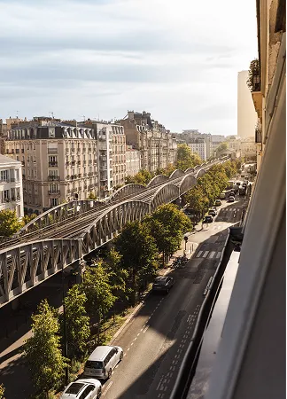Vue d'une rue parisienne avec un métro aérien, voitures et bâtiments Haussmanniens ensoleillés.