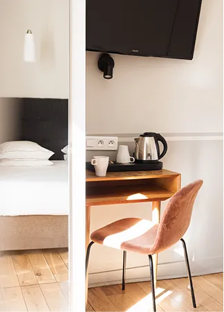 Coin bureau avec chaise rose, bouilloire, tasses et TV au-dessus à côté d'un lit blanc.
