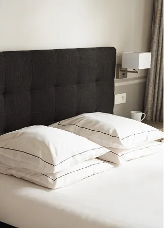 Lit avec tête de lit noire et quatre coussins blancs sur un matelas blanc.