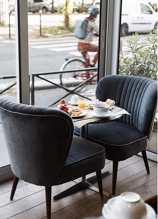 Table with breakfast items between two chairs by a window showing a cyclist passing outside.