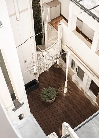 Vue plongeante sur une cour intérieure avec plancher en bois, plantes et éléments décoratifs suspendus.