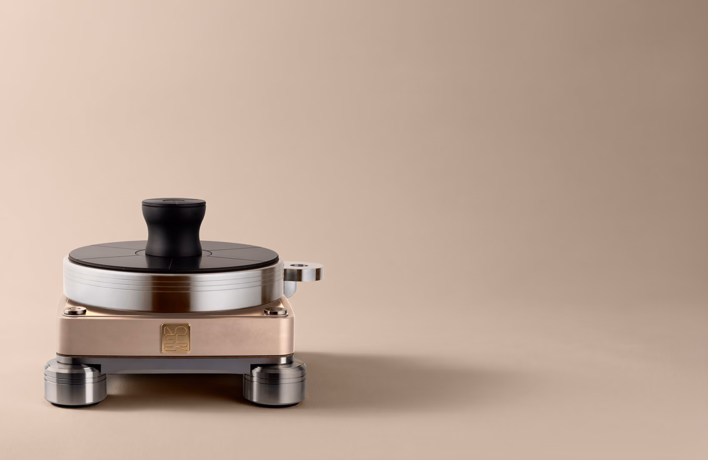 Dispositivo audio metallico compatto con manopola nera superiore e base color bronzo su fondo beige.