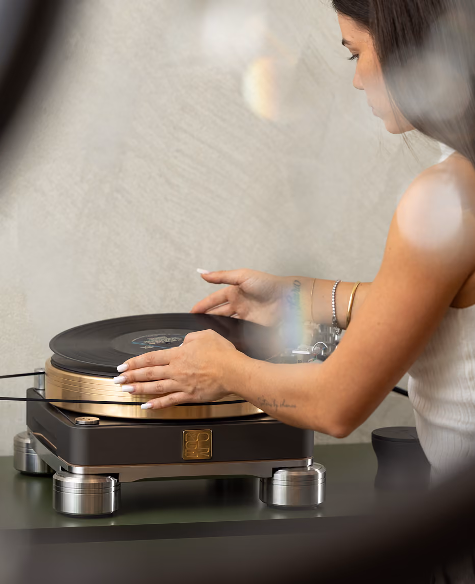 Donna con capelli scuri con smalto bianco sulle unghie, che maneggia un vinile su un giradischi moderno con base nera e dettagli metallici.