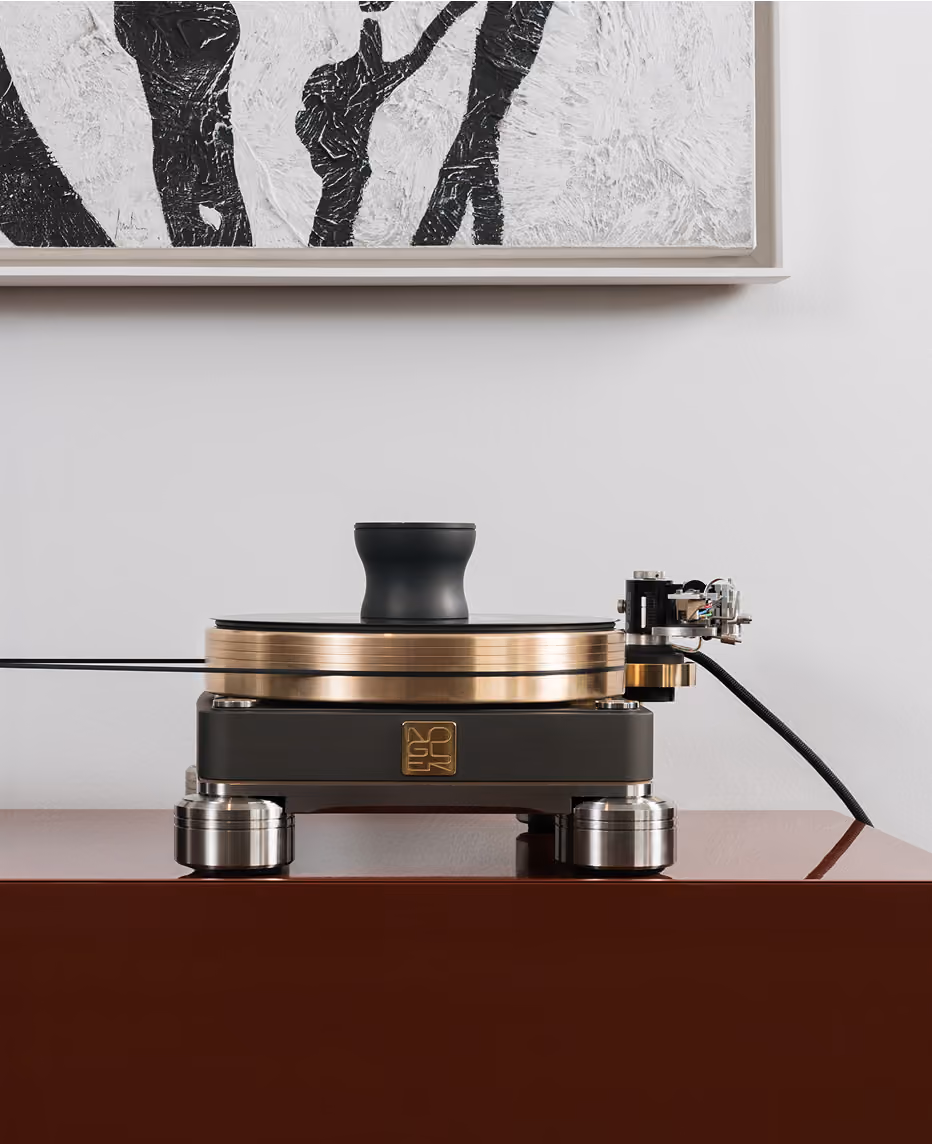 Giradischi di design moderno con struttura nera, piatto color oro e parti metalliche lucide, posizionato su mobile marrone lucido sotto un quadro astratto bianco e nero.