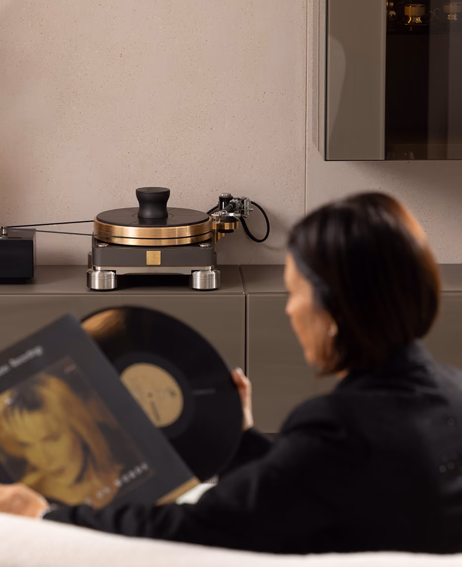 Una persona di spalle che tiene un disco in vinile mentre si trova di fronte a un giradischi moderno su un mobile in una stanza elegante.