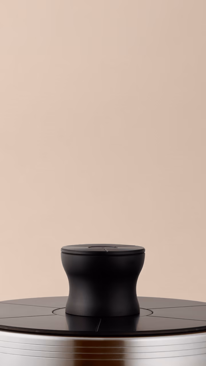 Close-up of a small black cylindrical object with a slightly hourglass shape placed on a dark circular surface against a beige background.