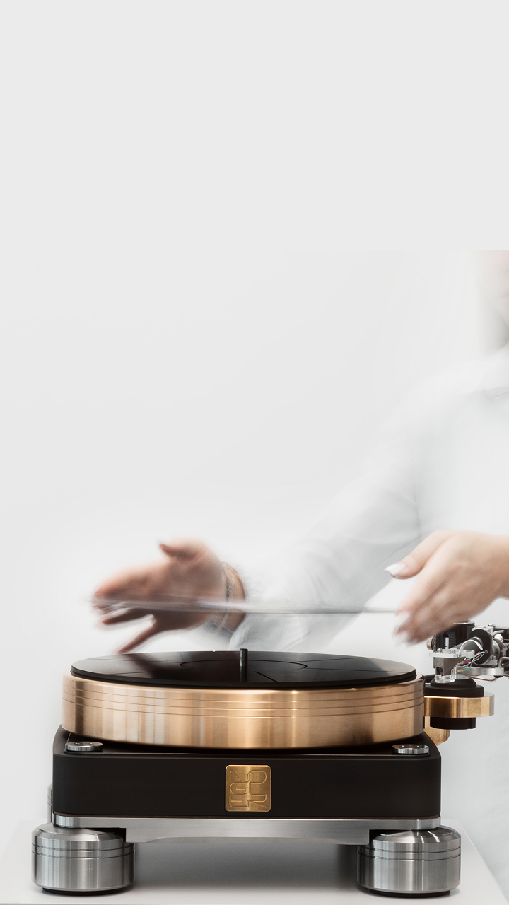 Giradischi moderno con base nera e dettagli in oro rosa, con una persona sfocata che posiziona un disco in vinile trasparente.