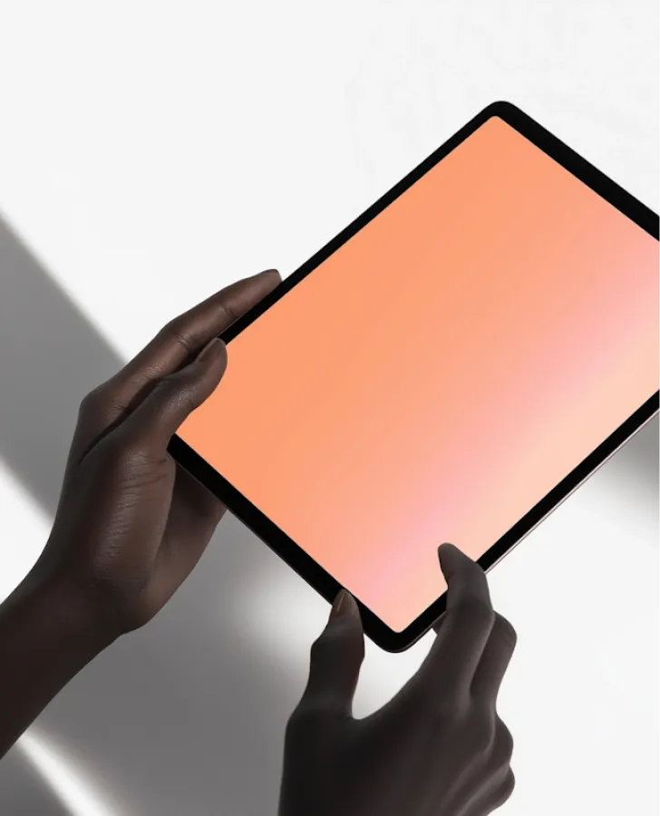 Two hands holding a tablet device with a blank peach-colored screen on a white surface.