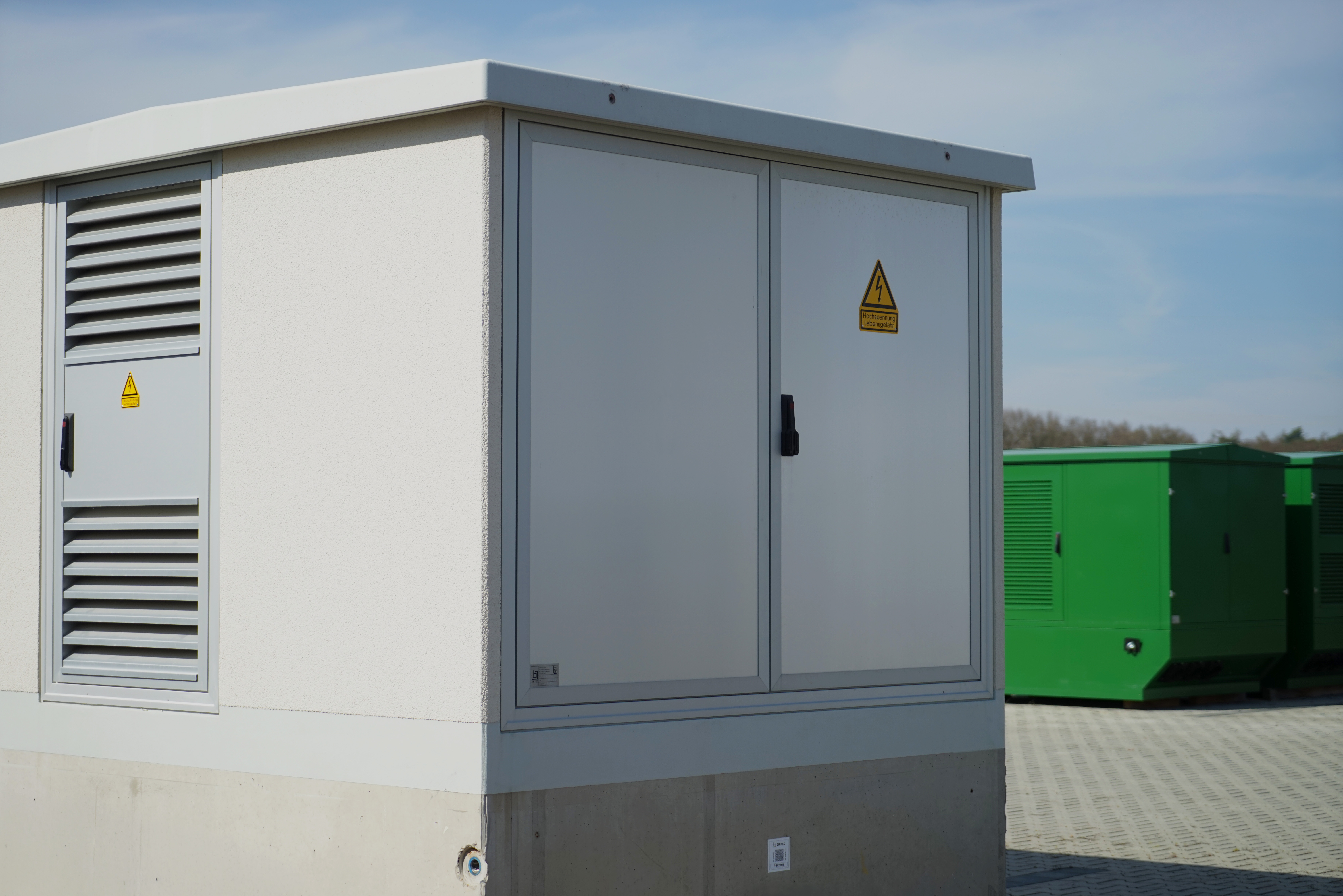 Kompakte Transformatorenstation mit Doppeltür und Hochspannungs-Warnschild im Freien