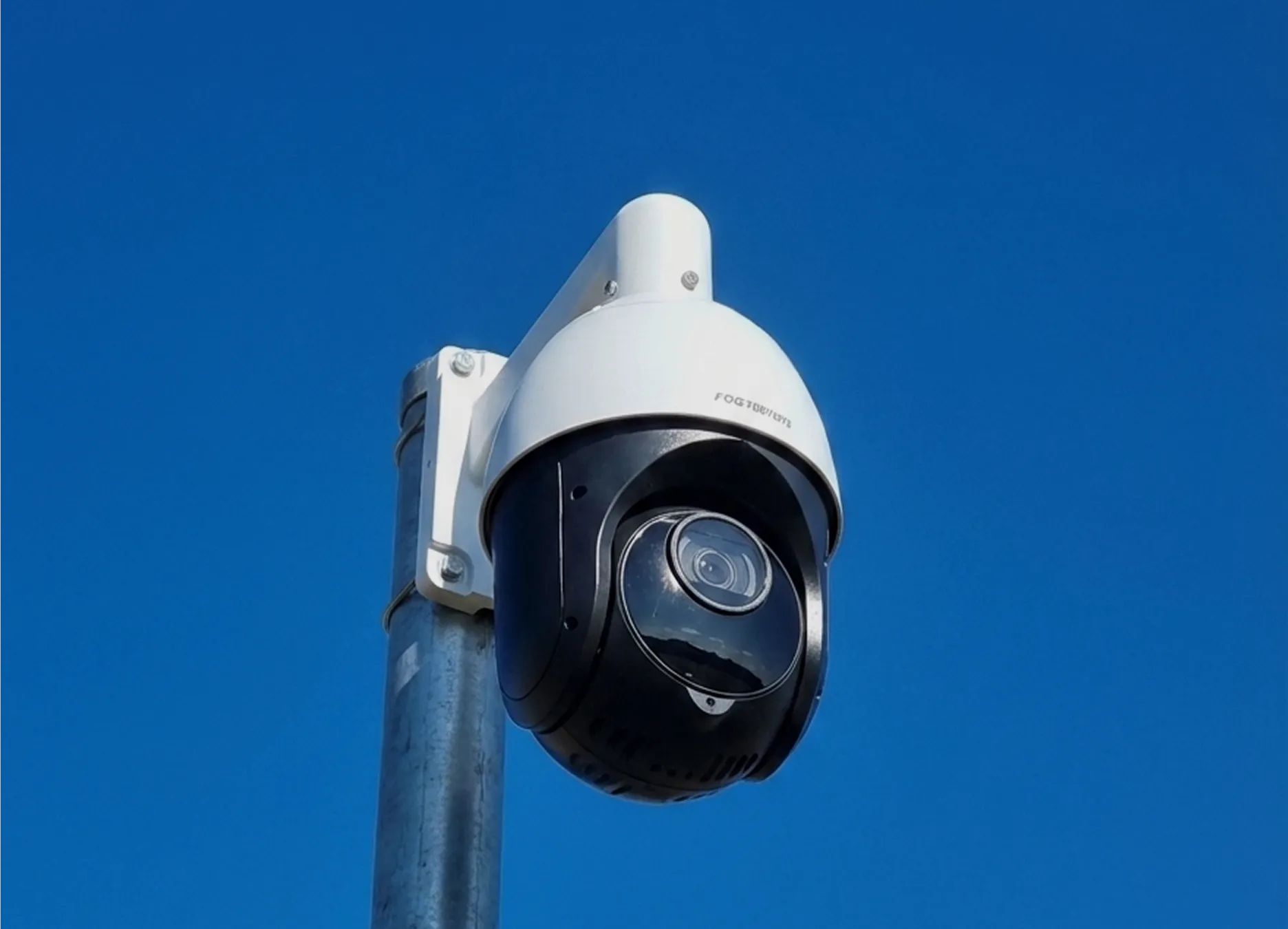 Security surveillance camera mounted on a metal pole against a clear blue sky.
