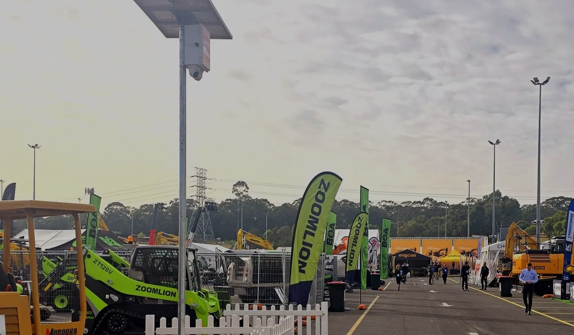 Outdoor construction equipment display with Zoomlion flags and people walking on a paved lane.