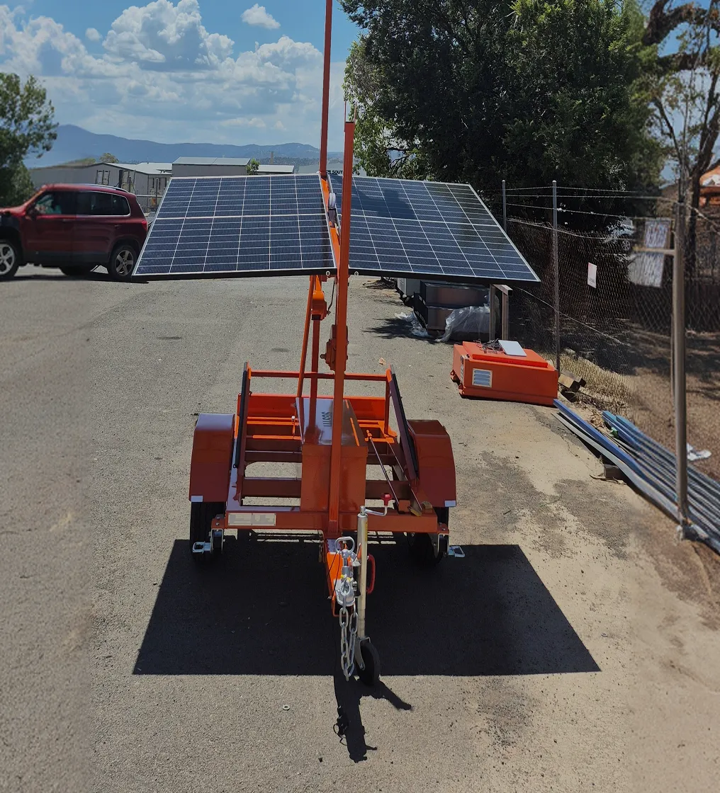 Mobile orange trailer fitted with two solar panels on an adjustable arm in an outdoor industrial setting.